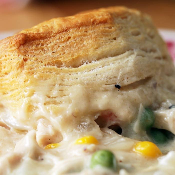 Closeup of a flaky biscuit atop a creamy mixture of chicken, corn, peas, and carrots