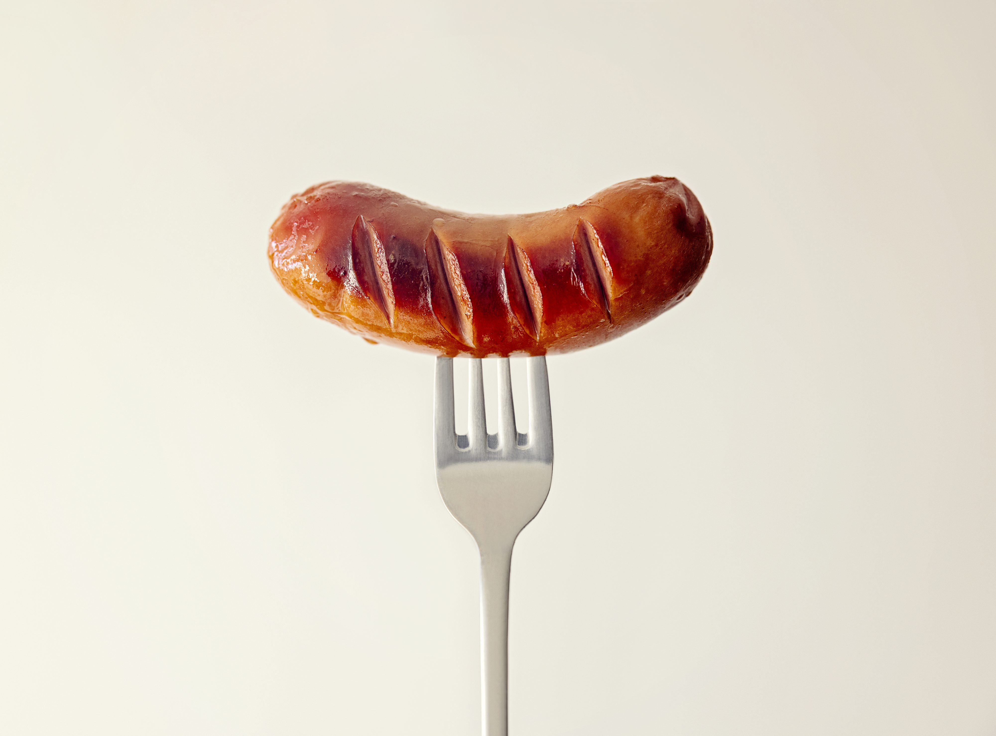 A grilled sausage pierced with a fork, held upright against a plain background