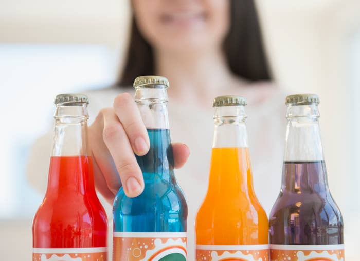 A person reaches for one of four soda bottles in different colors displayed on a table