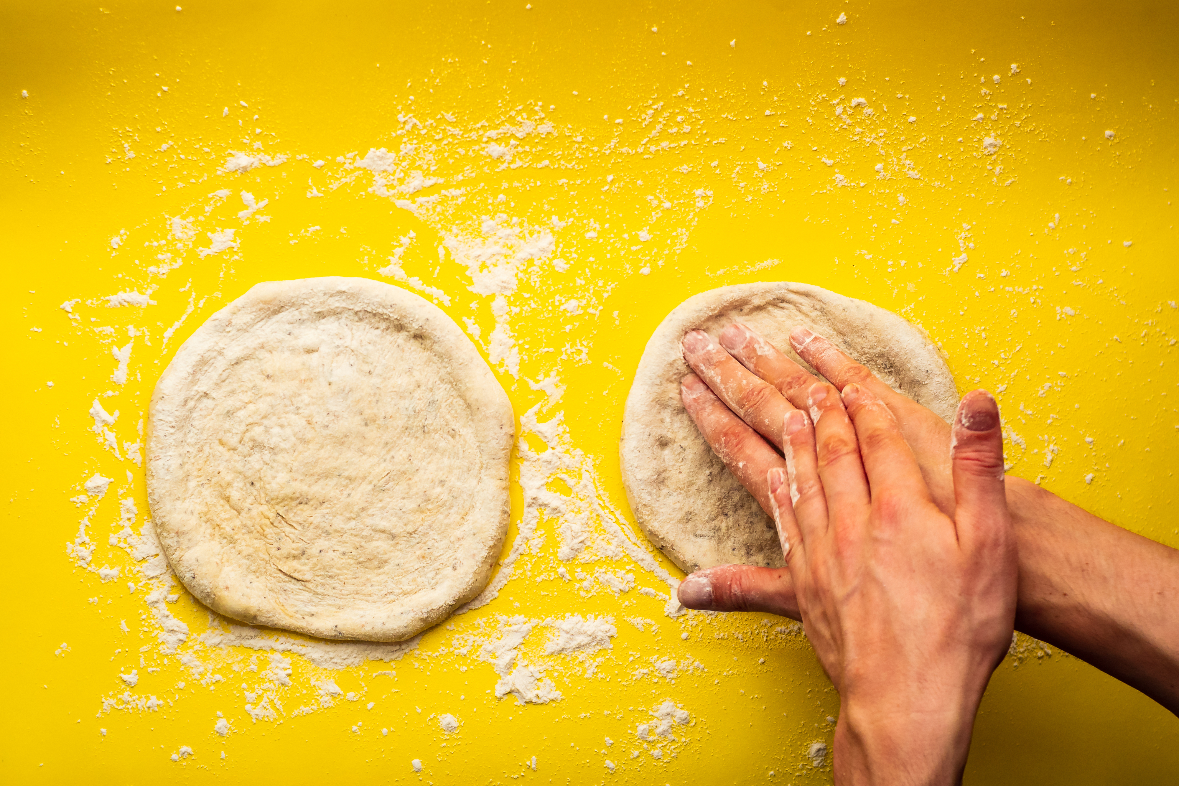 Hands shaping pizza dough on a flour-dusted surface, preparing bases for baking
