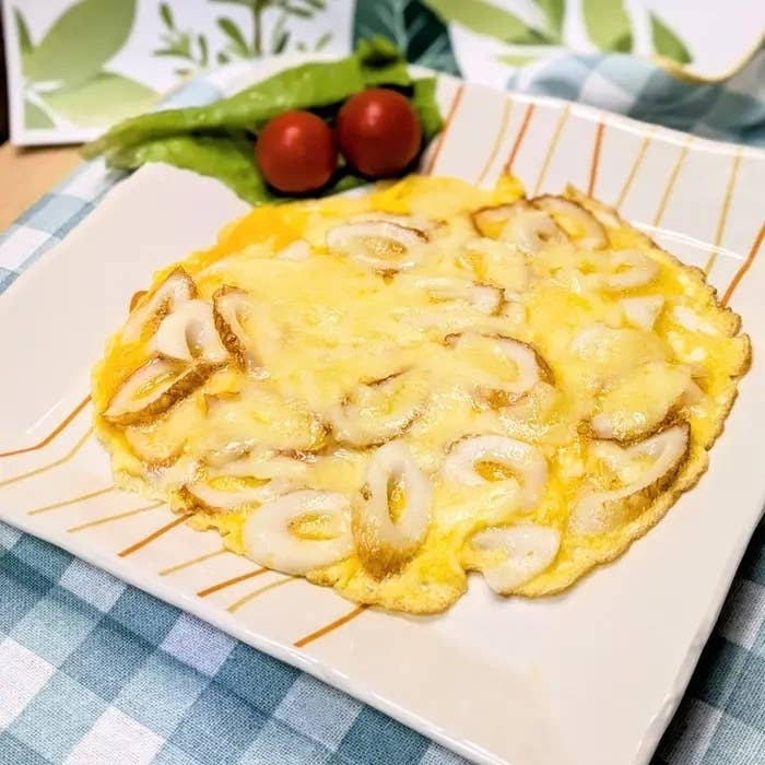 オムレツにチーズとカットしたイカがトッピングされた料理。背景にチェリートマトとレタスが添えられています。