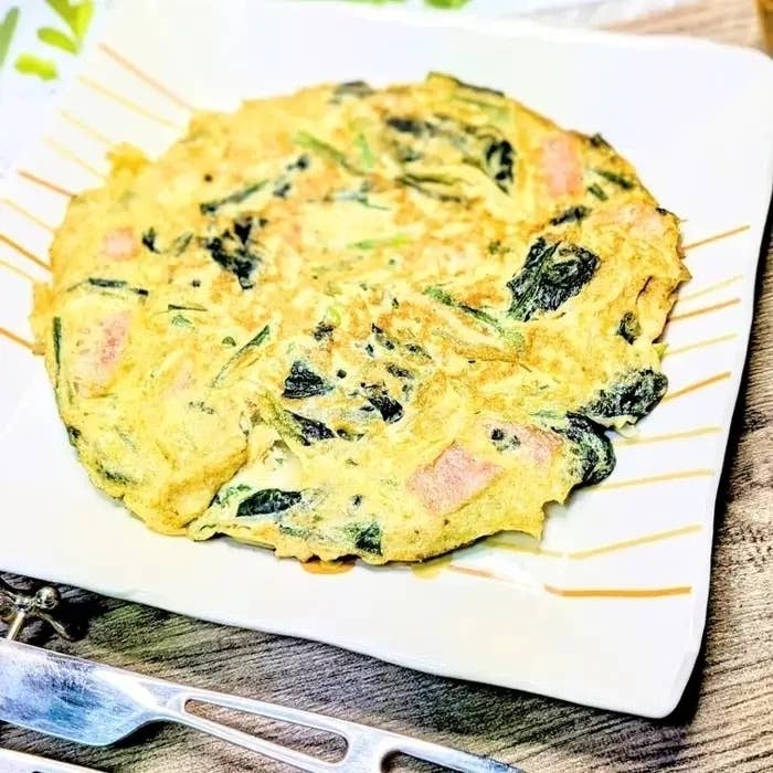 お皿に盛られた韓国料理のチヂミ。具材には野菜とハムが含まれている。