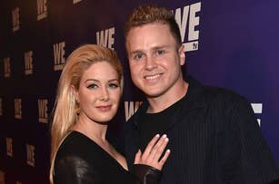 Two people pose together at a WE TV event. One is wearing a black outfit with leather accents; the other is in a dark button-up shirt