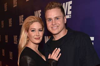 Two people pose together at a WE TV event. One is wearing a black outfit with leather accents; the other is in a dark button-up shirt
