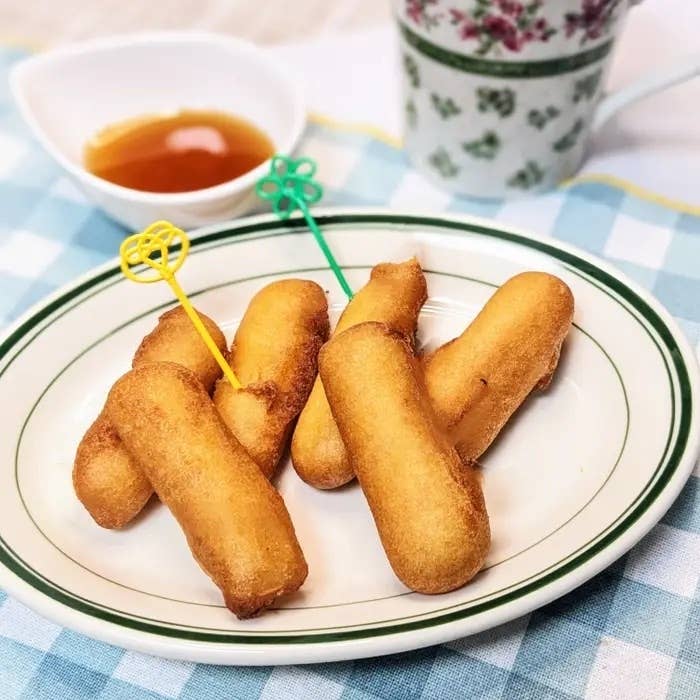 お皿に盛られたドーナツに似た揚げ菓子が並んでおり、蜂蜜が添えられている。背景にカップが見える。