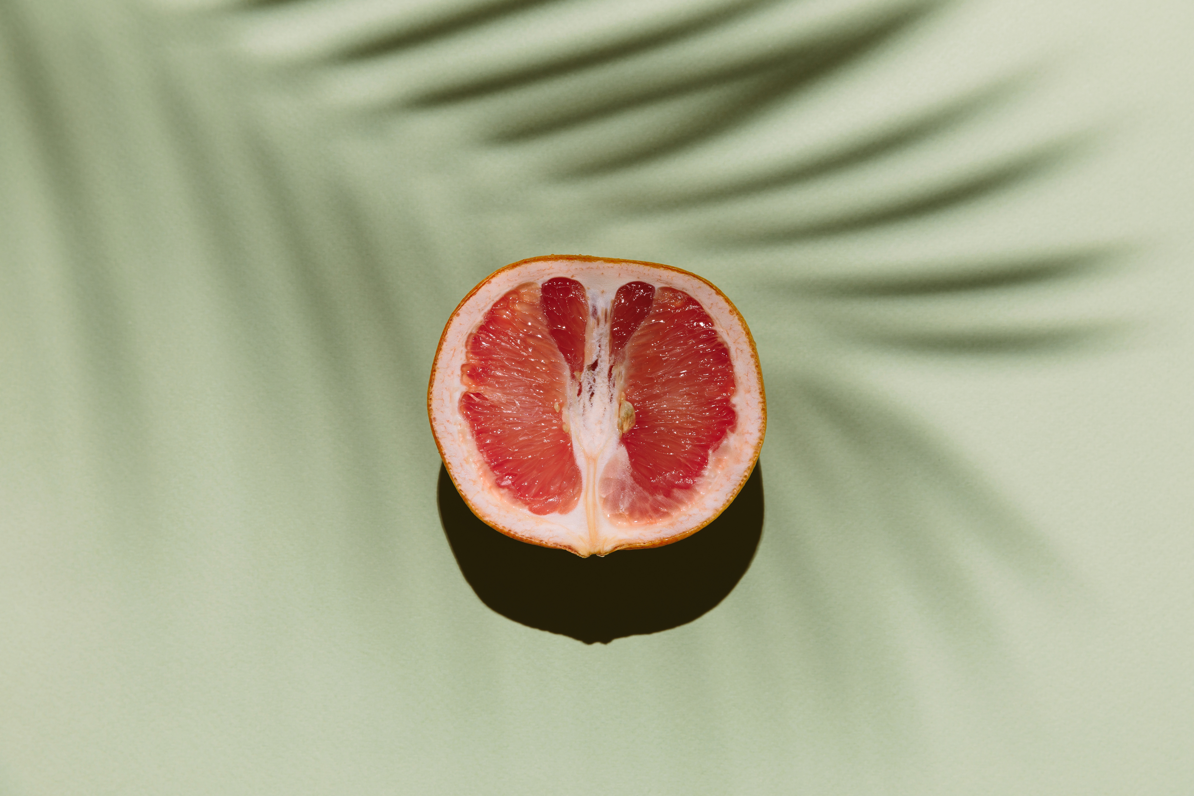 En halv grapefrukt sitter på en glatt overflate med palmebladskygger, og fremkaller en rolig, minimalistisk estetikk
