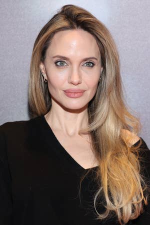 Angelina in a sweater with long, wavy hair poses with neutral expression against a plain background