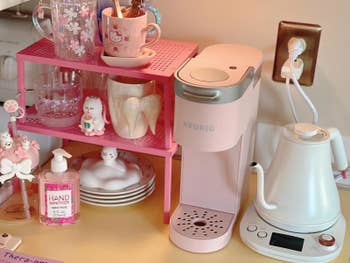 Coffee presumption with a pinkish Keurig, achromatic electrical kettle, mugs, and manus sanitizer