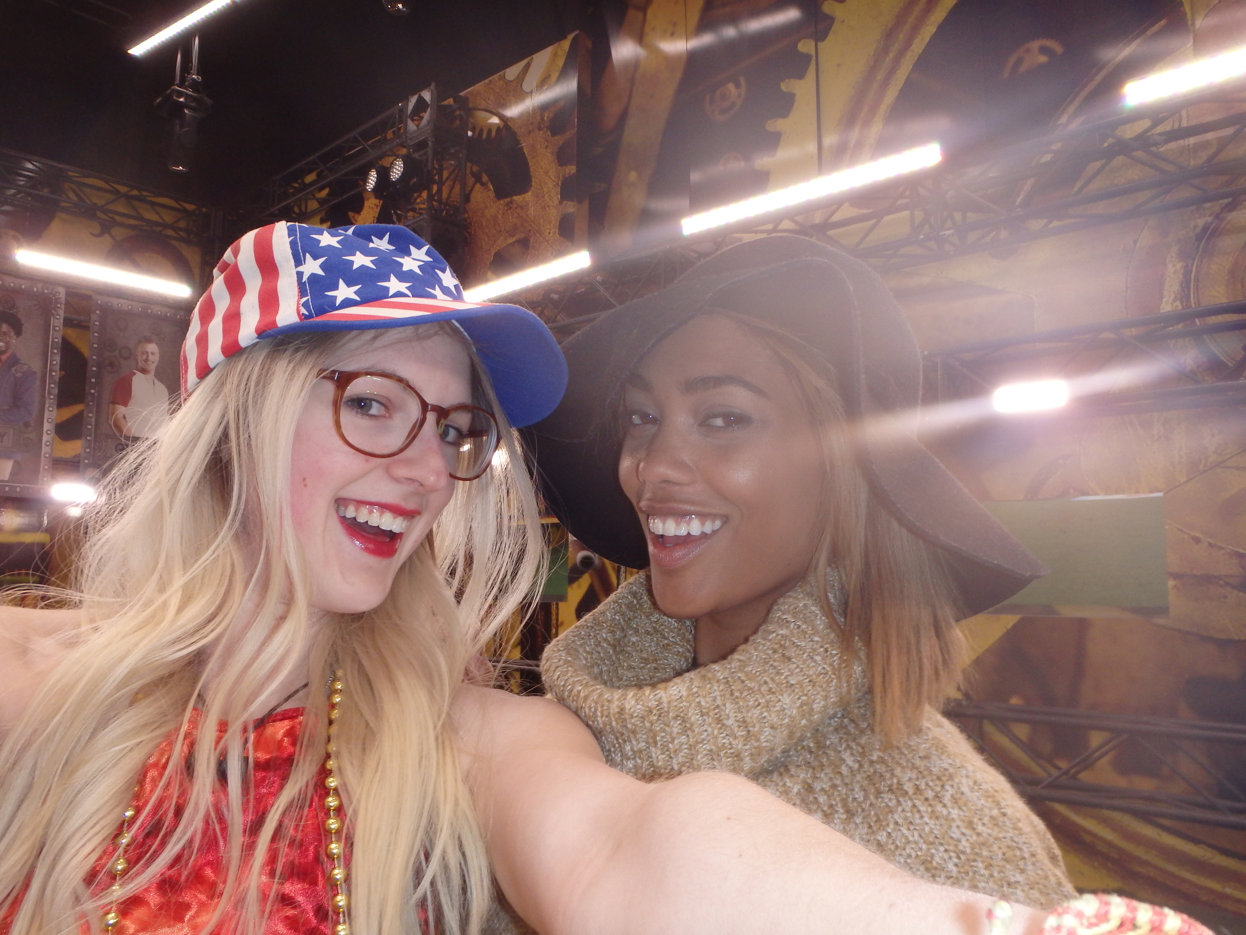 Two smiling people taking a selfie. One wears a star-patterned cap and glasses; the other has a wide-brimmed hat and a cozy sweater