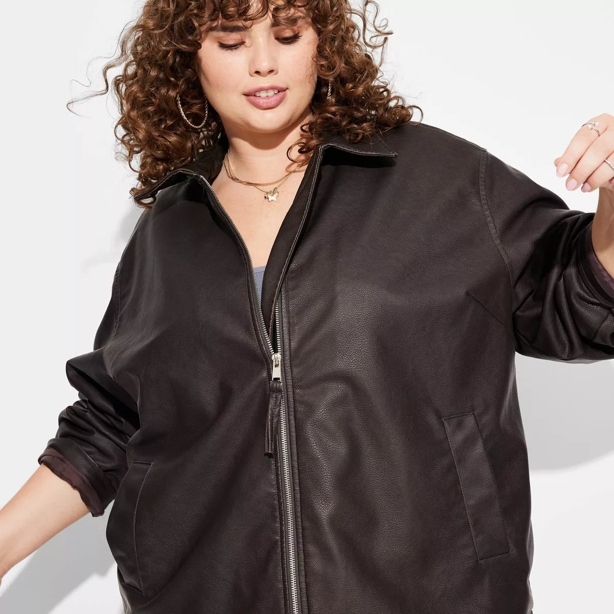 Person wearing a stylish leather jacket, curly hair, and hoop earrings, looking downward