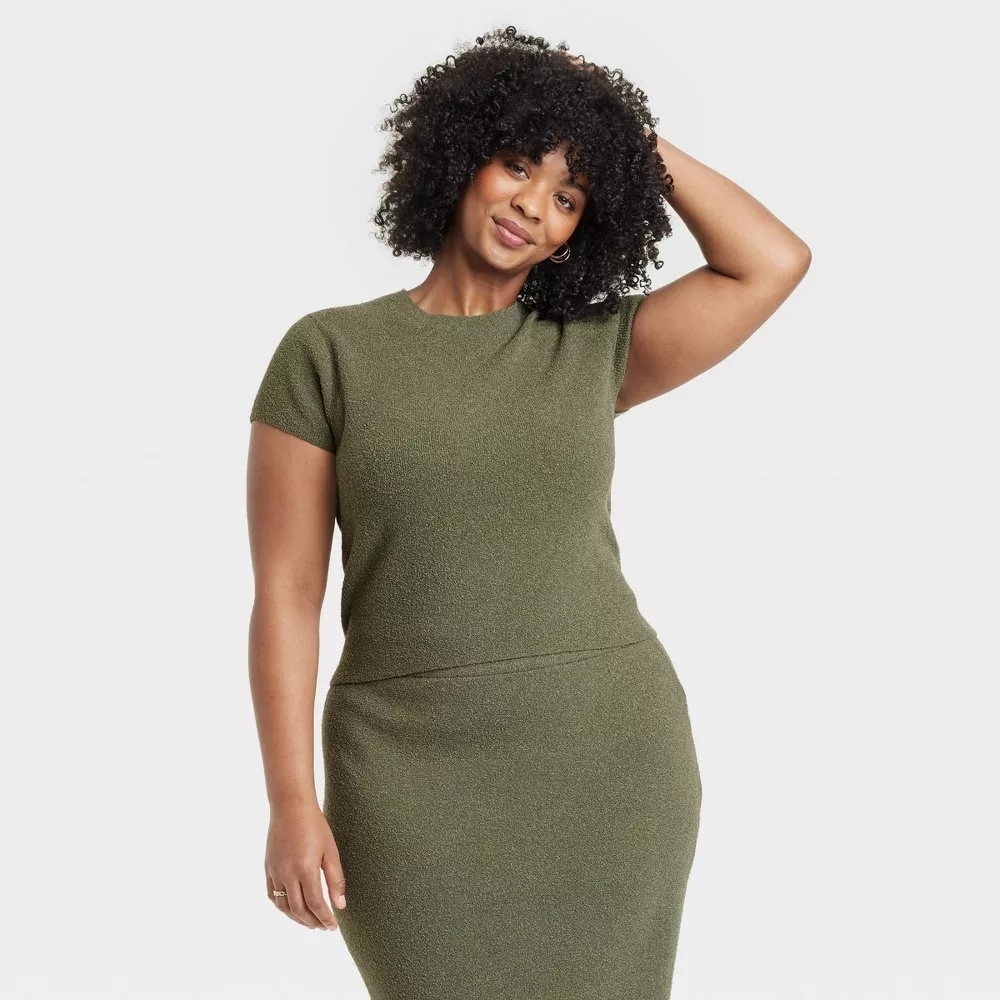 Woman in fitted, short-sleeve dress poses confidently with one hand on her hip and the other touching her curly hair. Shopping category image