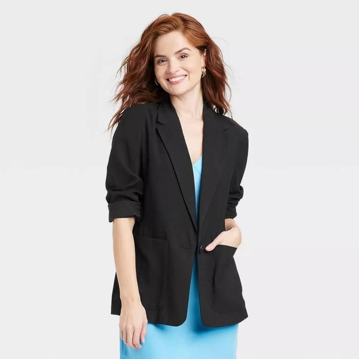 Person wearing a stylish black blazer over a blue dress, posing and smiling