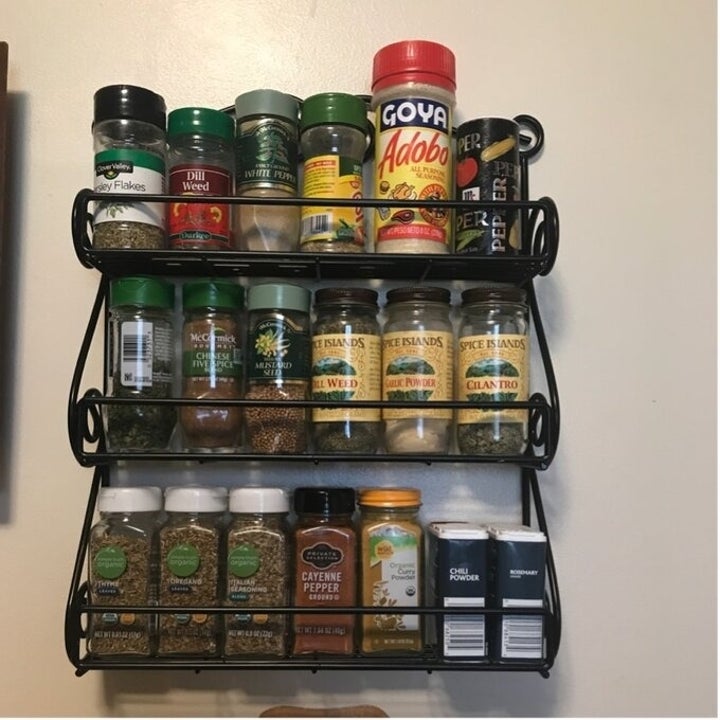 Wall-mounted spice rack filled with various spice jars, including garlic powder, cayenne pepper, and dill weed