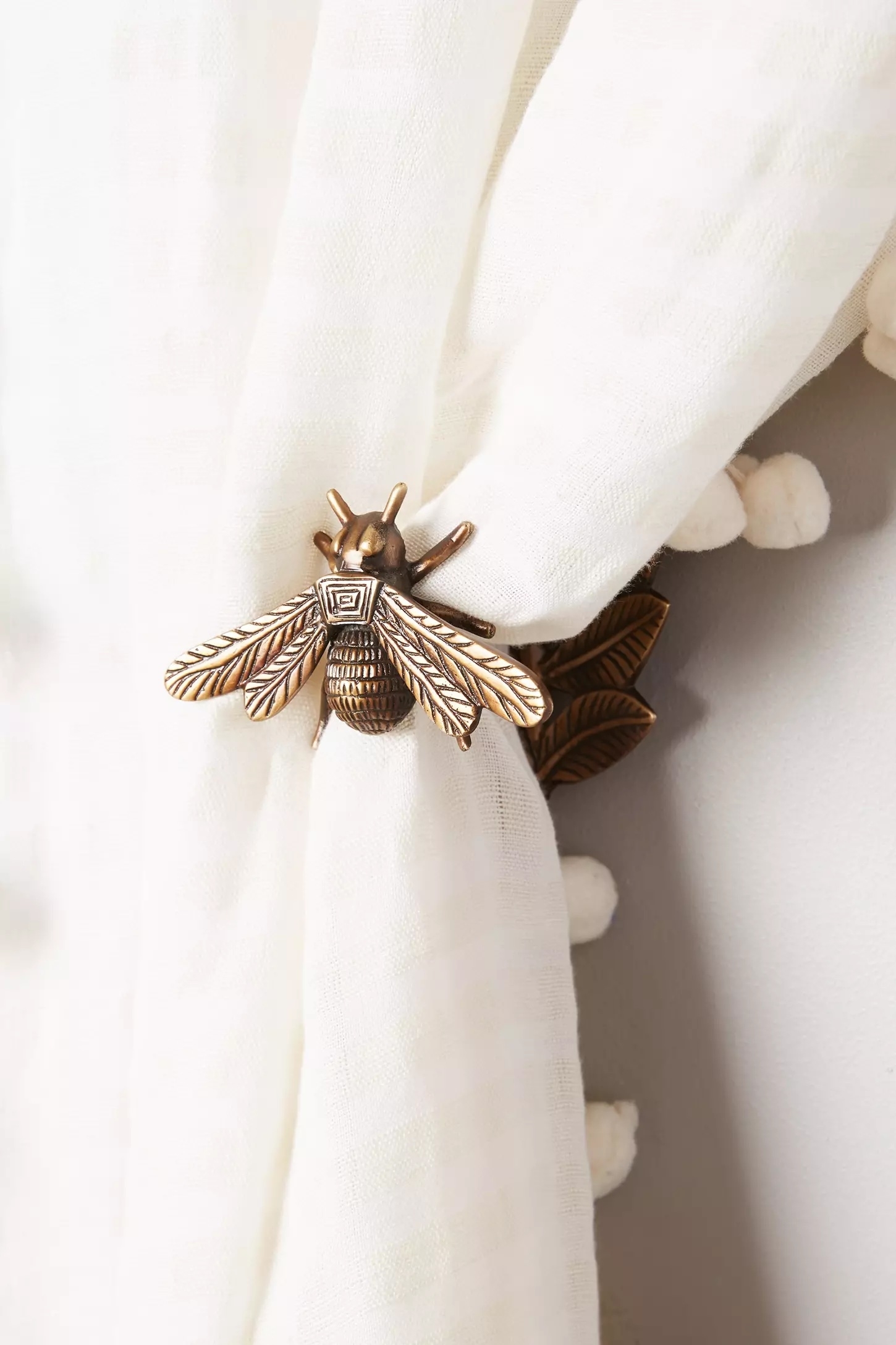 Bee-shaped curtain tie-back holding white fabric with textured details. Ideal for adding a whimsical touch to home decor