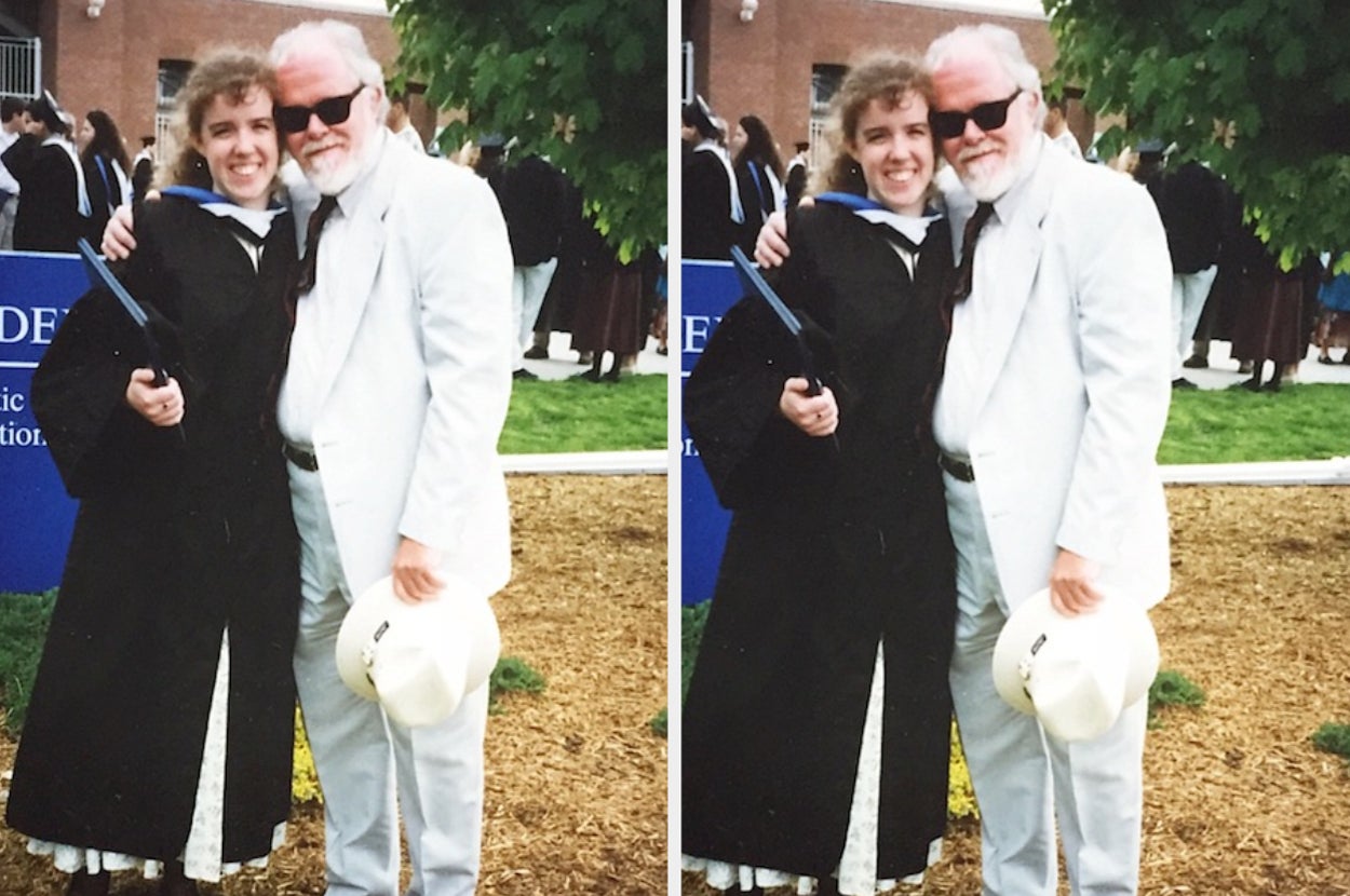 Two people in graduation attire stand outdoors, smiling and posing closely. One is holding a diploma cover, and the other is wearing a light suit and holding a hat