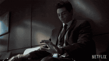 Noah Centineo sits on a chair, dancing in his seat while drumming his palms on his knees