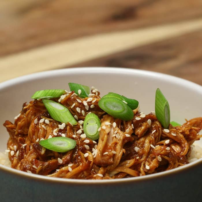 Bowl of shredded chicken seasoned with sesame seeds and sliced green onions, served over rice