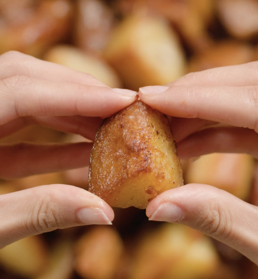 Close-up of hands holding a golden, crispy roasted potato