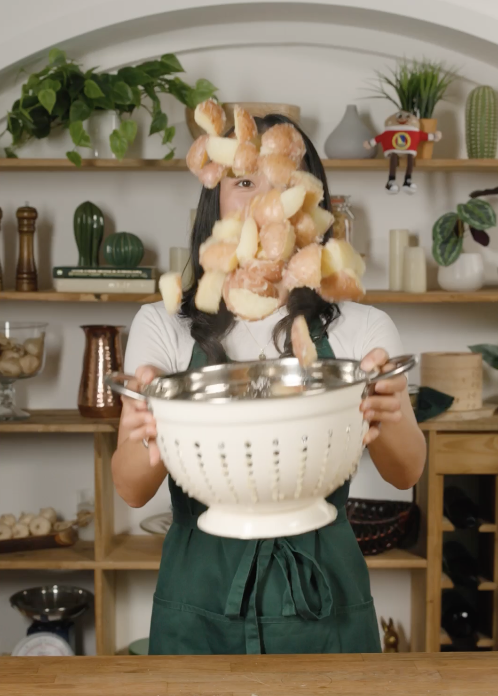 Person tossing chunks of peeled potatoes successful  a colander successful  a room  mounting  with shelves successful  the background