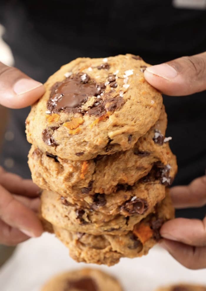 Hands holding a stack of 4  chunky cookies with cocoa  chips and a sprinkle of brackish  connected  top