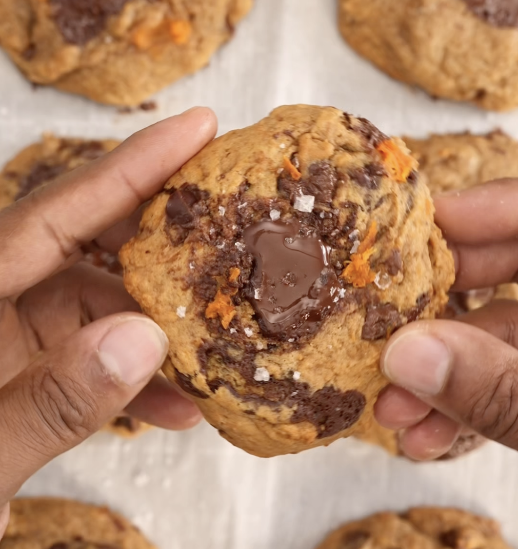 Person holding a freshly baked cocoa  spot   cooky  with a gooey center, surrounded by much  cookies connected  a baking sheet