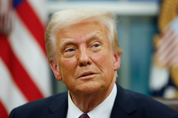 男性がスーツを着て座っている。背景にアメリカ国旗が見える。