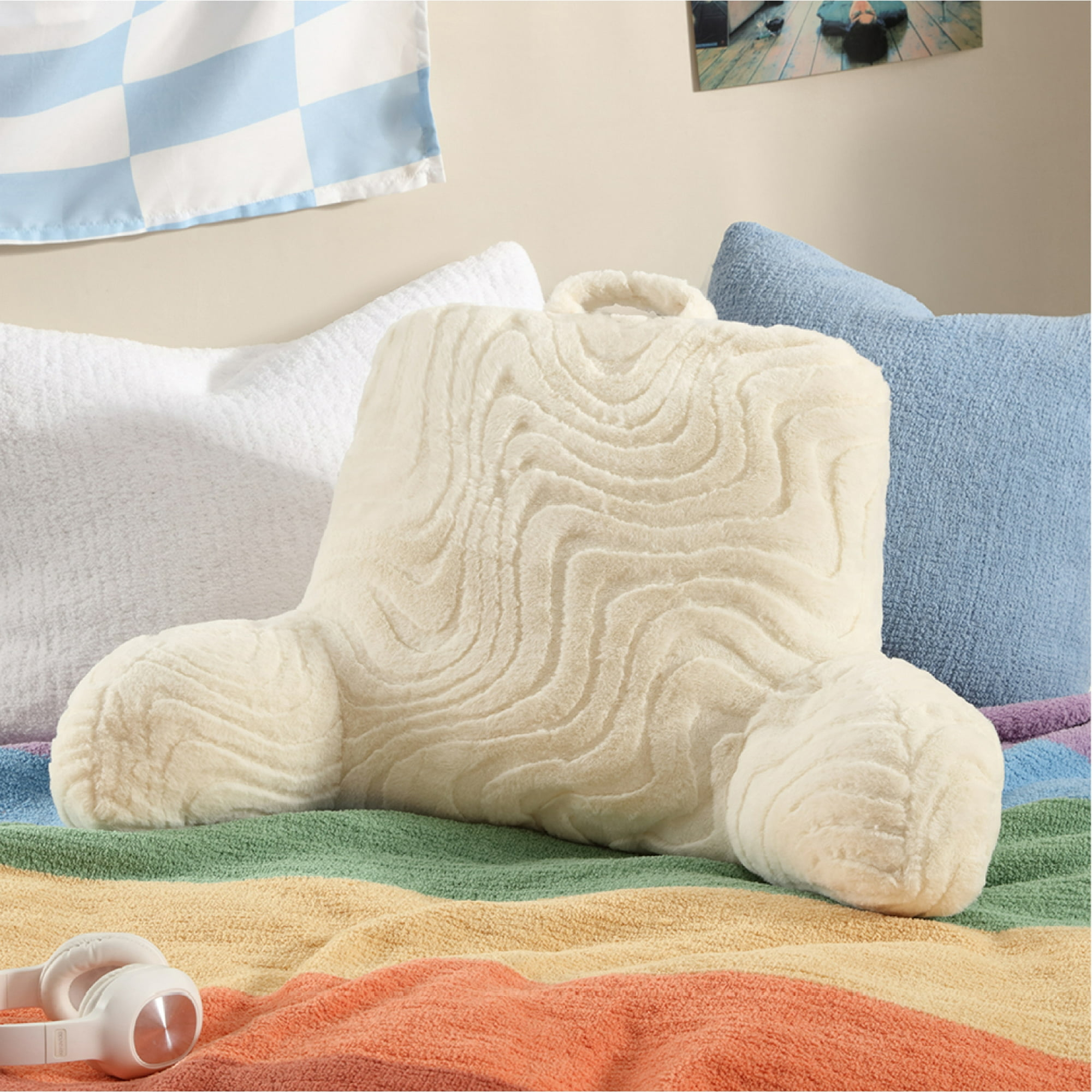 Plush, textured pillow shaped for back support on a bed with a striped rainbow blanket and headphones nearby