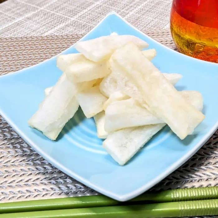 青い皿に盛り付けられた数枚のサツマイモのフライと、横に置かれた飲み物のガラス。