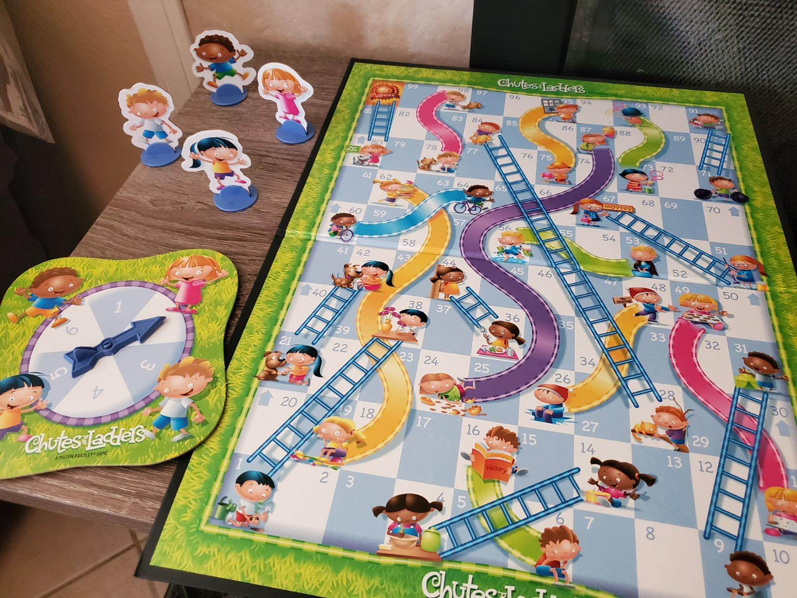 A Chutes and Ladders board game is set up with cartoon child-themed pieces and a spinner on a table, ready for play