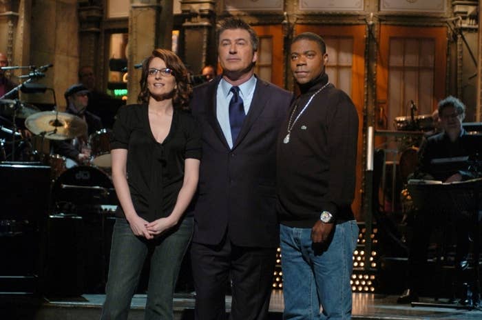 Three people stand on stage of a live TV show. One wears a suit, another jeans and a blouse, and the third a casual top with jeans