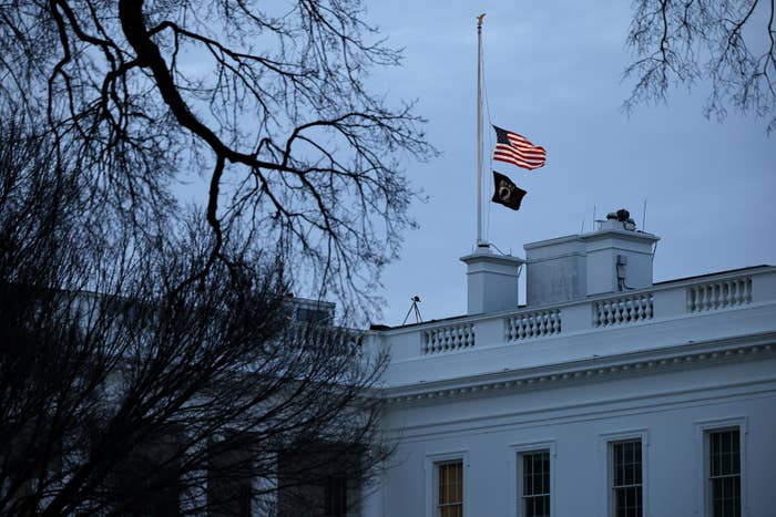 American flag at half-mast on the White House surrounded by leafless trees
