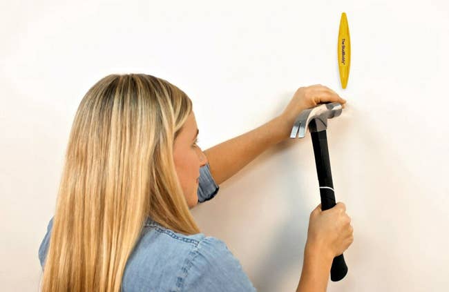 Model using a hammer and a wall hook guide to hang an item on a wall, demonstrating a simple home improvement task