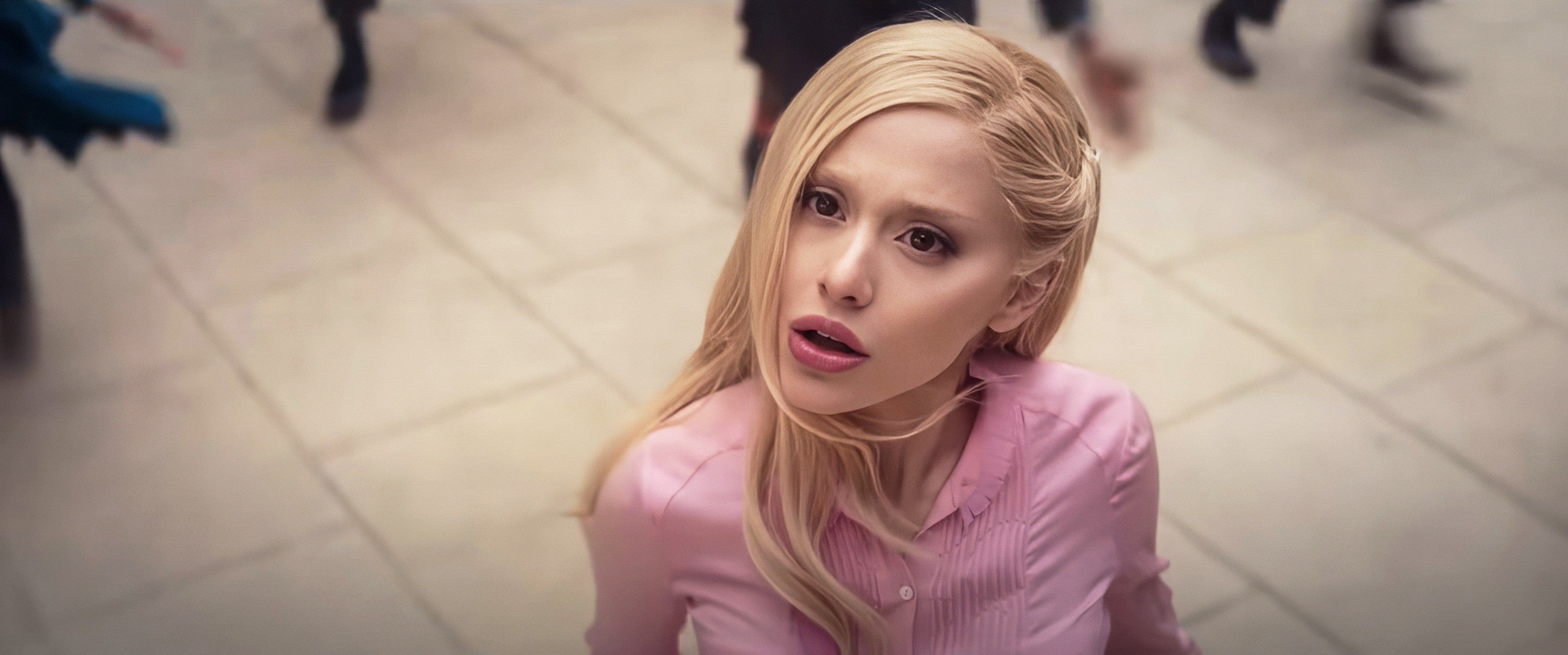 Person with long hair in a pink blouse looking upwards, appearing surprised or confused