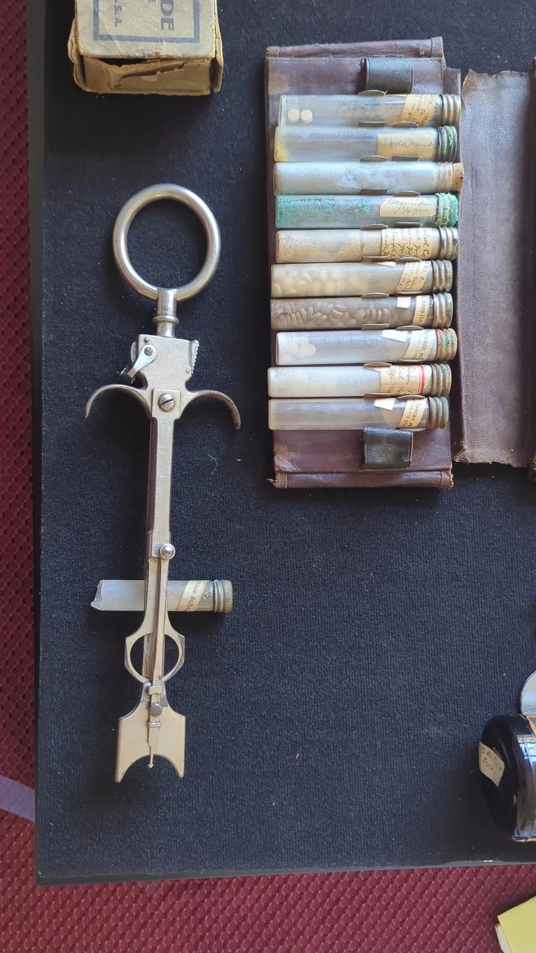 Antique tool with a handle similar to a syringe and an end with sharp metal implements with multiple glass tubes on display