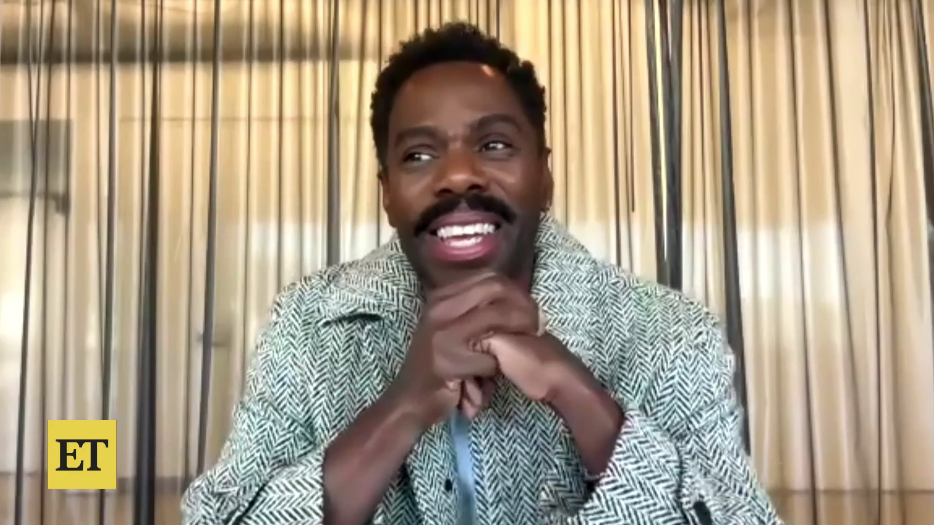Colman Domingo wearing a patterned jacket smiles, clasping hands