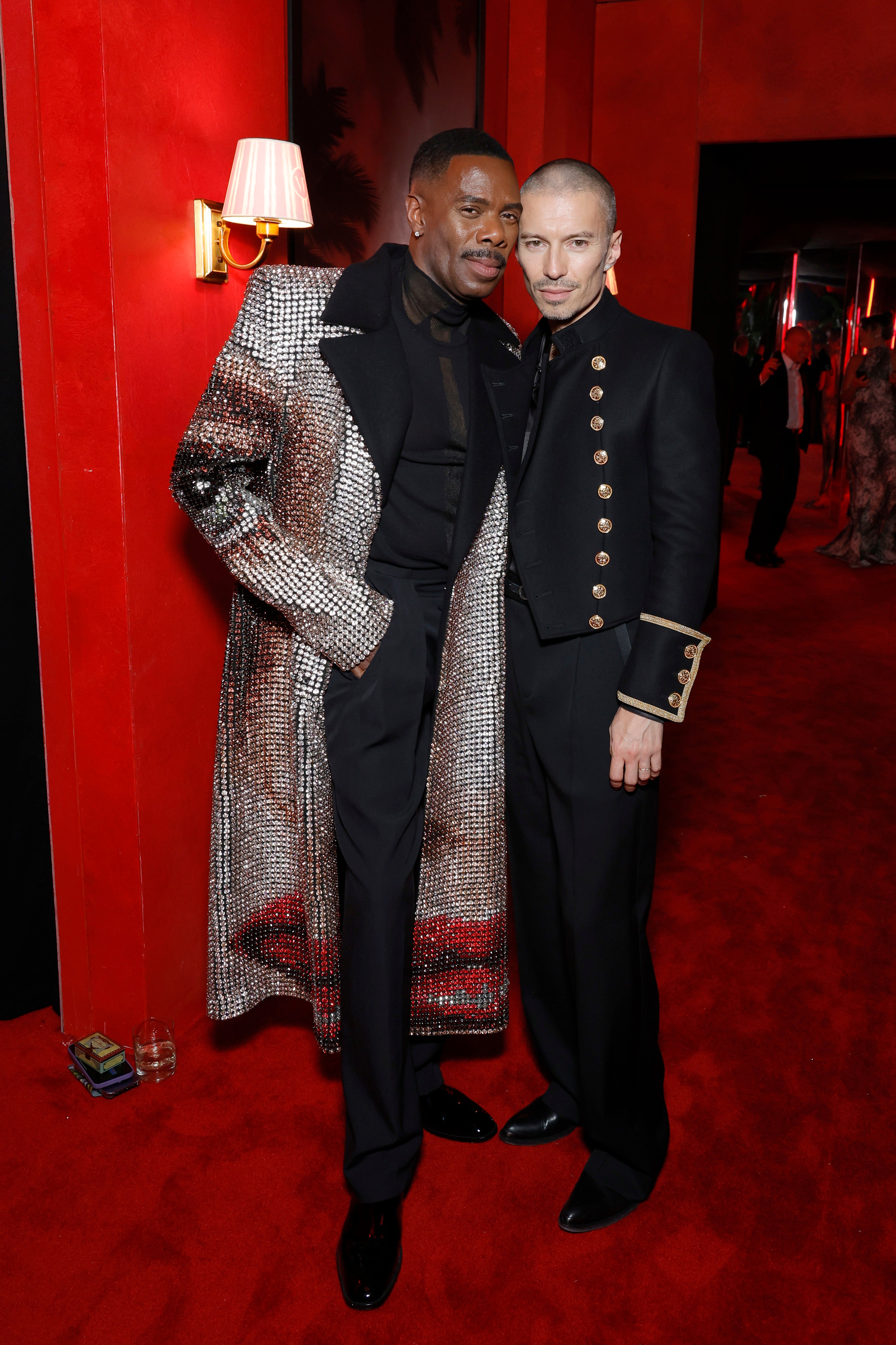 Colman Domingo and his husband, Raúl on the red carpet, one wearing a sparkling coat over a dark outfit, the other in a black military-style jacket with gold buttons