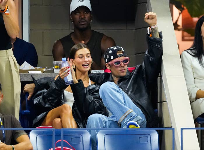 Hailey and Justin Bieber in casual attire sit in a stadium