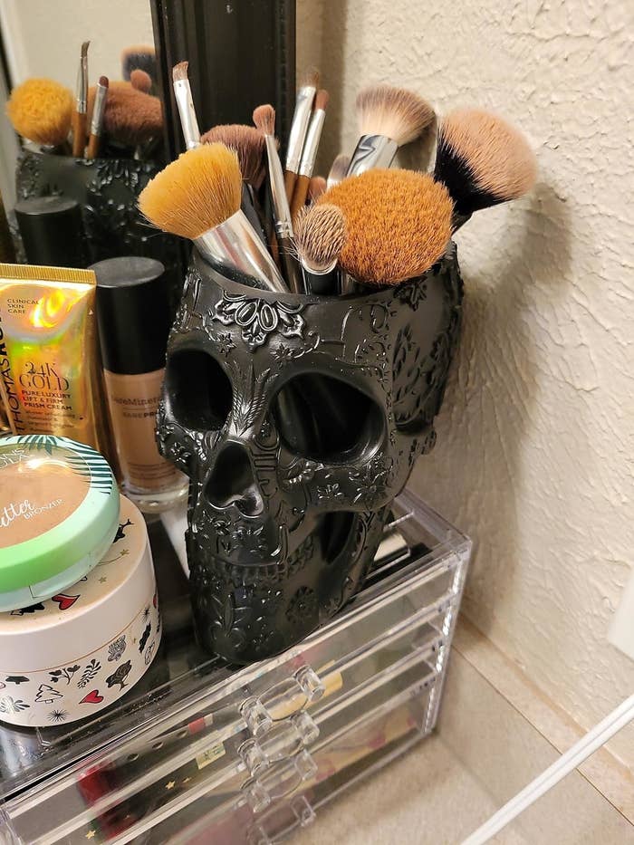Makeup brushes successful  a decorative skull holder connected  a vanity, surrounded by assorted  cosmetics and a wide   retention  organizer
