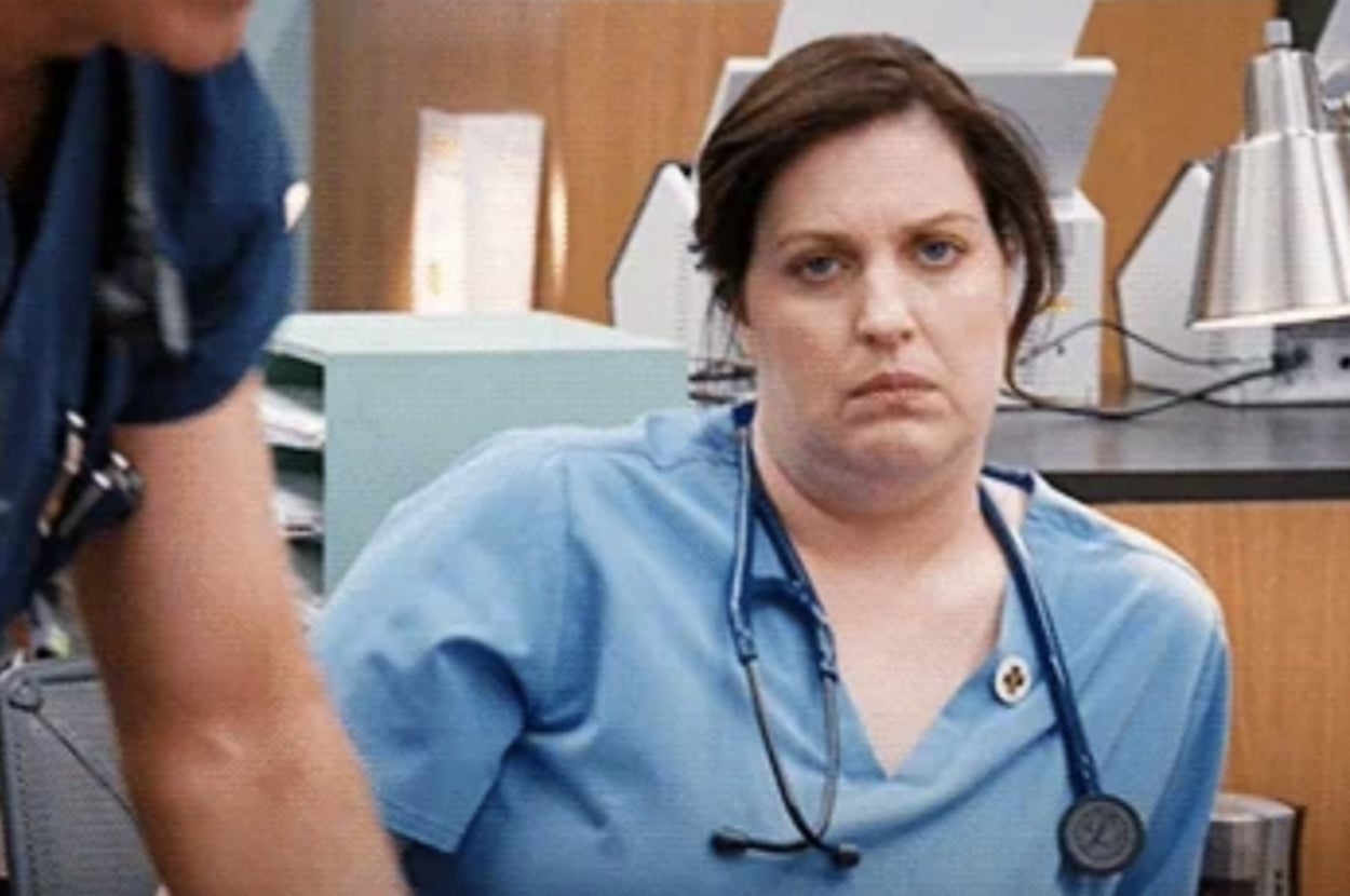 Person in a hospital setting wearing scrubs and a stethoscope, looking unimpressed