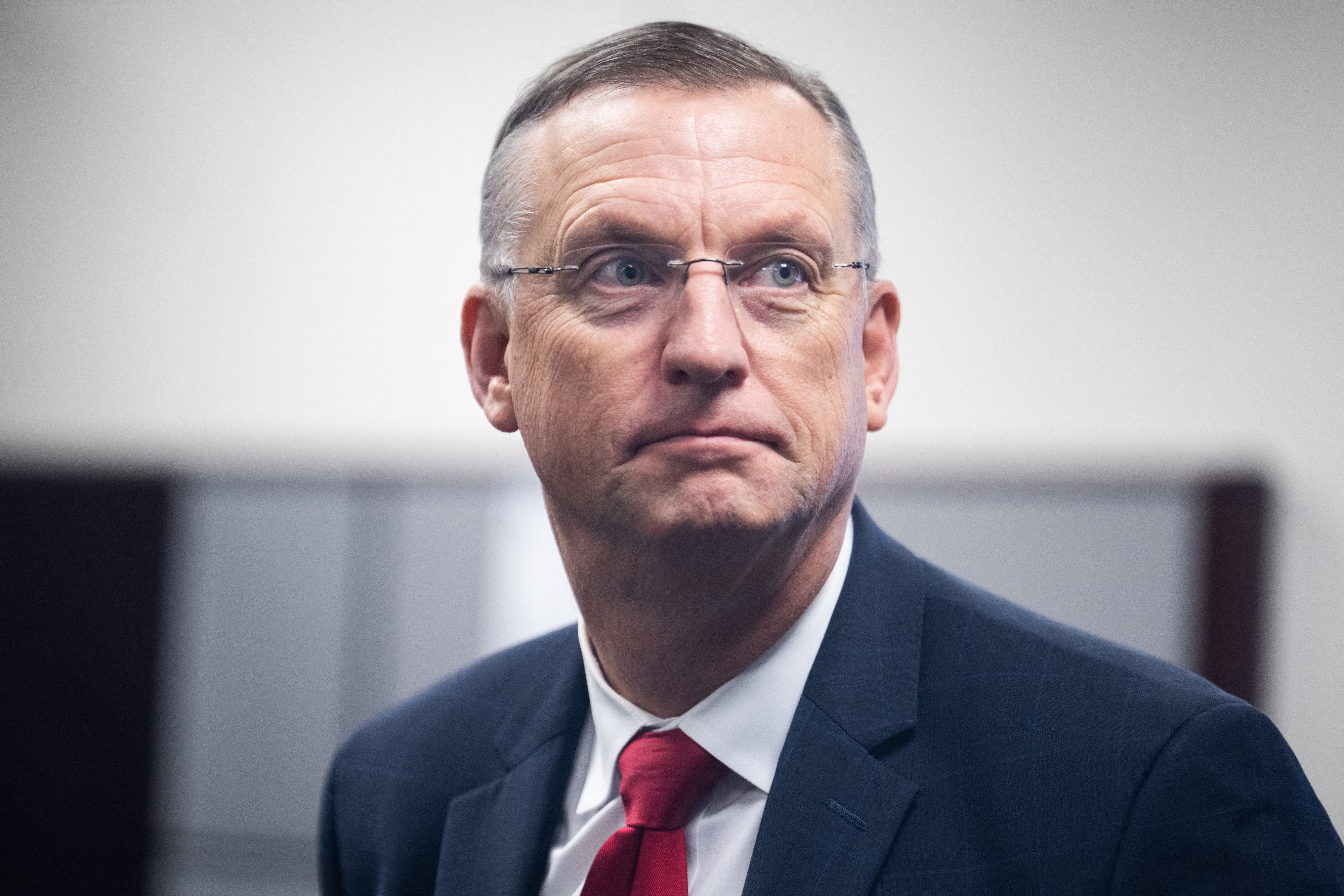 Douglas Collins in a suit and tie looks to the side in a formal setting