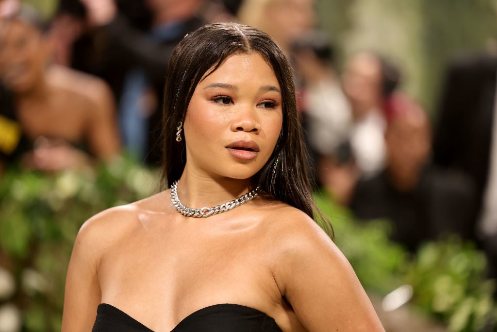 Woman on red carpet in elegant strapless gown with sleek hair, wearing a silver necklace and earrings, surrounded by event attendees