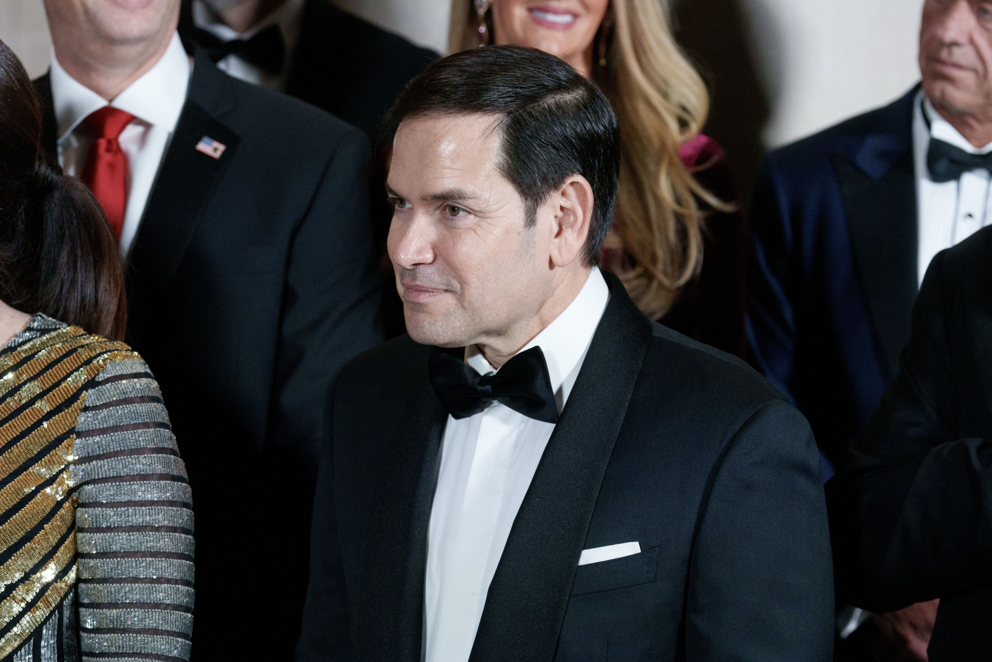 Marco Rubio in a tuxedo at a formal event, surrounded by people in elegant attire