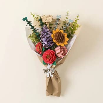 Bouquet of woody flowers including a sunflower, reddish roses, and lavender with greenish accents, wrapped successful brownish insubstantial and tied with a bow