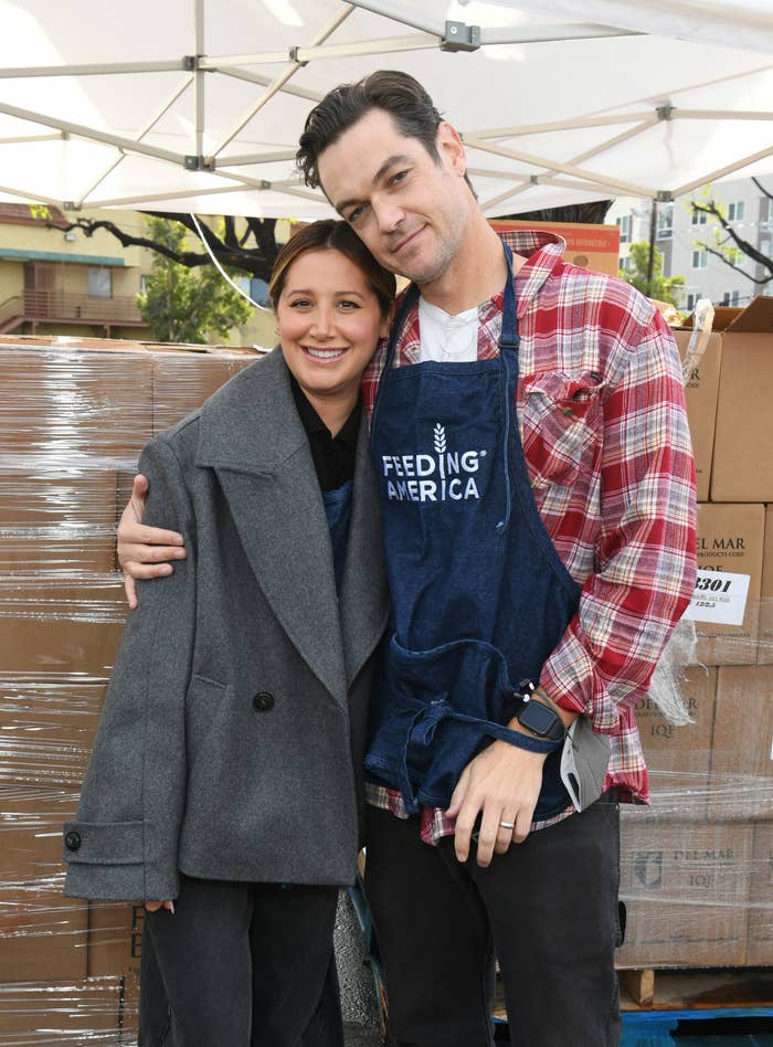 A smiling man and woman at a food charity event, the man wearing a 