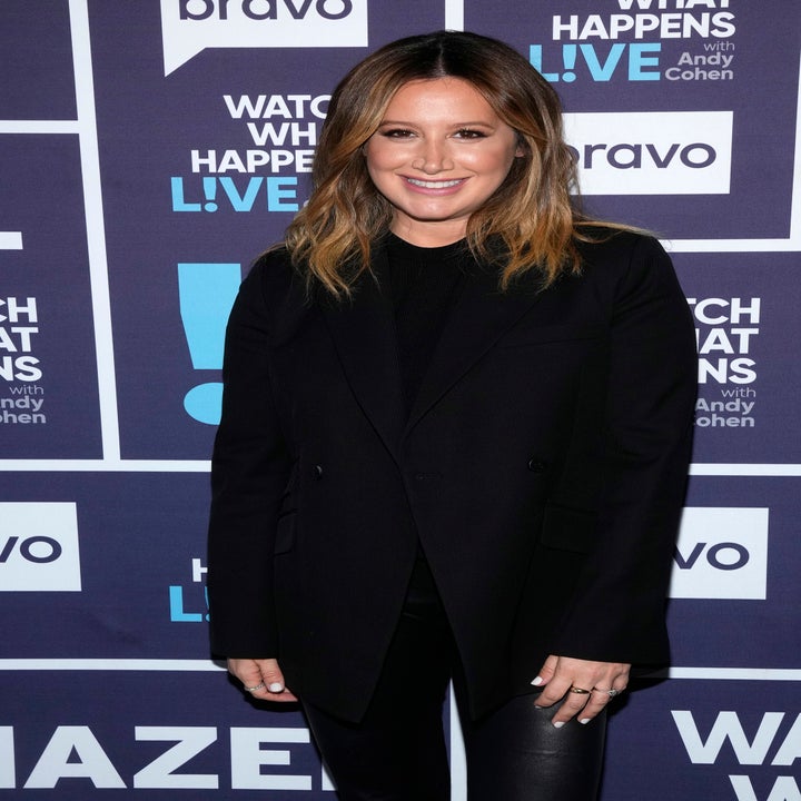 Person in a black outfit poses at a media event backdrop with "Watch What Happens Live with Andy Cohen" branding