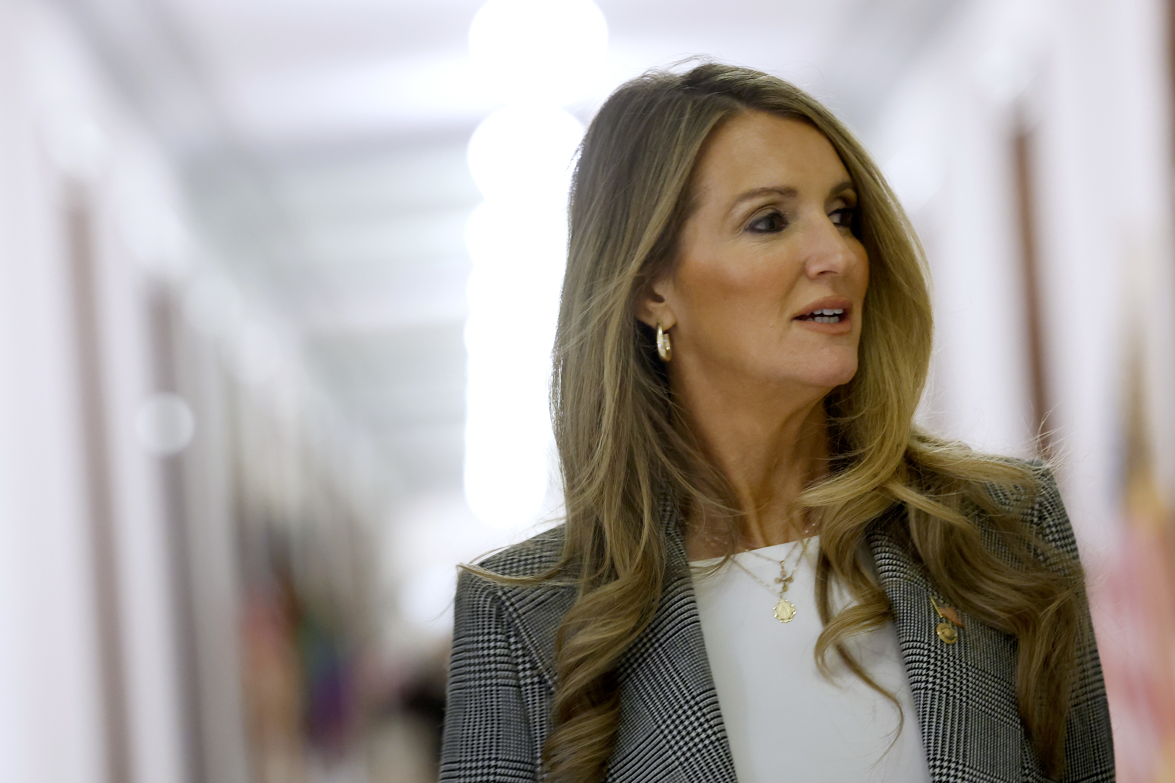 Kelly Loeffler  wearing a checkered blazer over a white top is looking to the side in a hallway