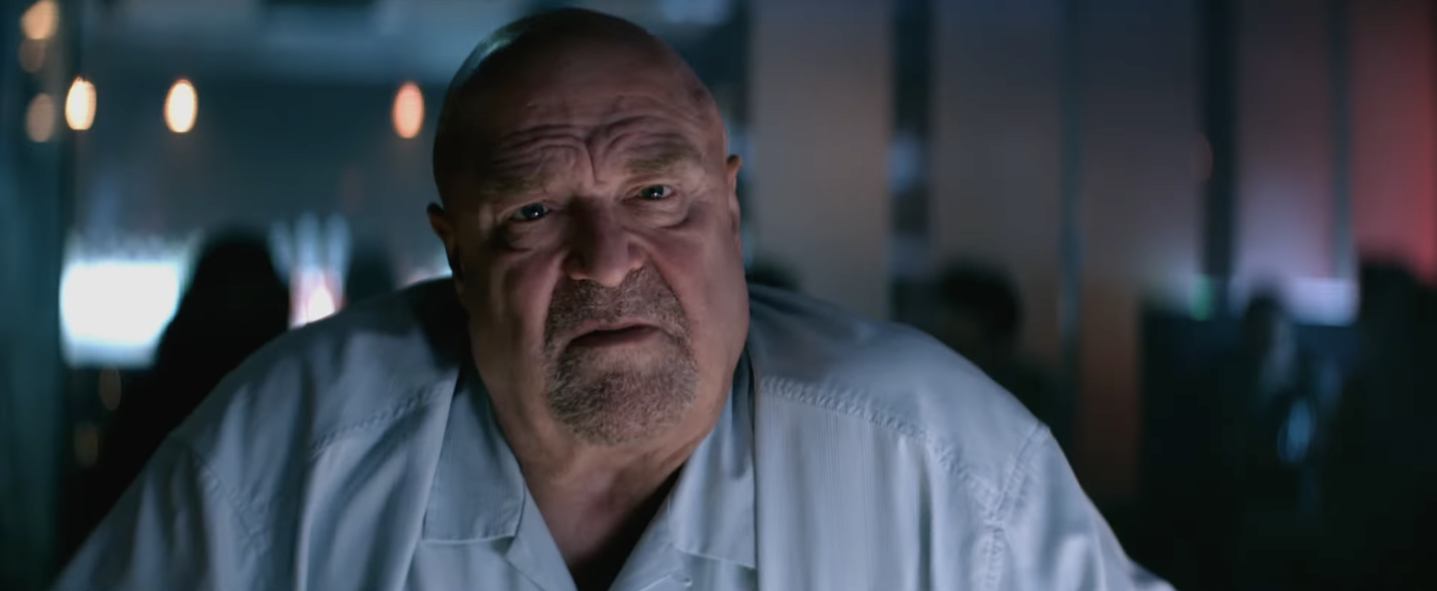Actor in a dimly lit room, wearing a casual button-up shirt, looking intensely at the camera