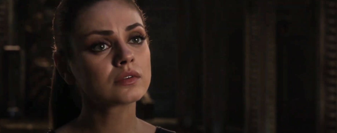Person in a film scene with a serious expression, looking slightly upward. Background appears dimly lit