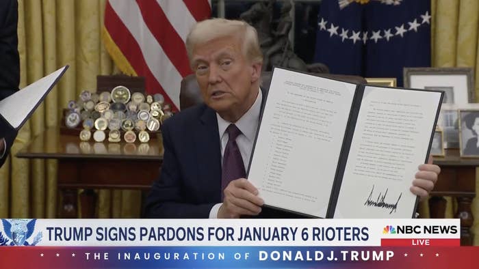 Man in suit holds open folder with document in an office. TV news banner reads: 