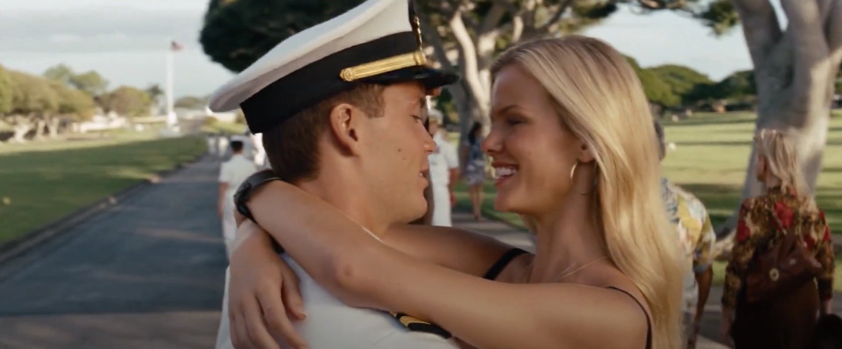 A couple embraces on a sunny day in a park; one wears a naval officer's uniform
